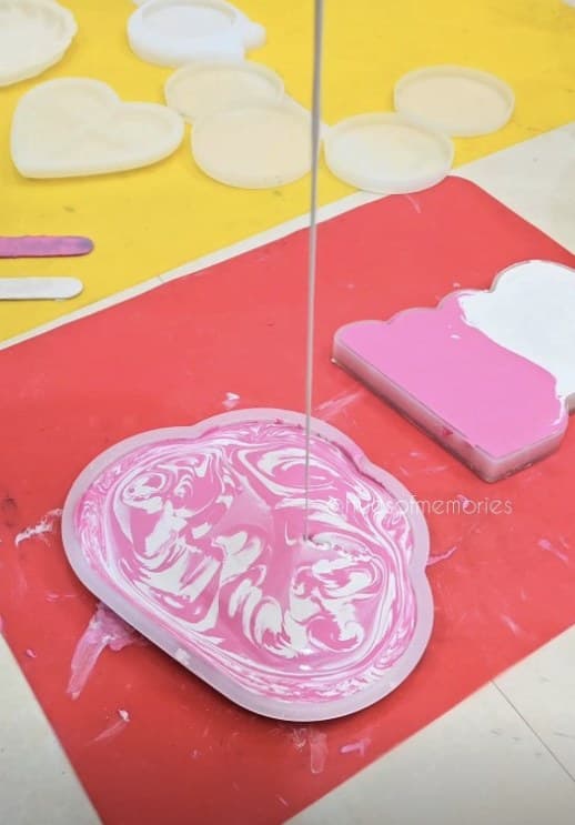 Pink and white marbled resin being poured into a tray mould